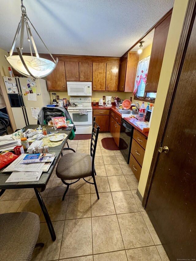 kitchen featuring white appliances, light tile patterned floors, brown cabinetry, and a textured ceiling