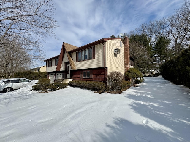 snow covered property featuring a garage, a chimney, and a wall unit AC