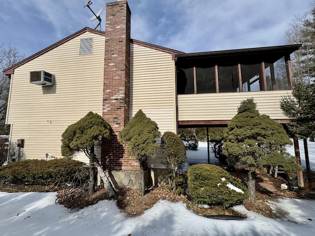 view of side of property with a chimney, a wall unit AC, and a sunroom