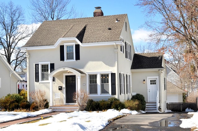 traditional home with a shingled roof, a chimney, fence, and stucco siding