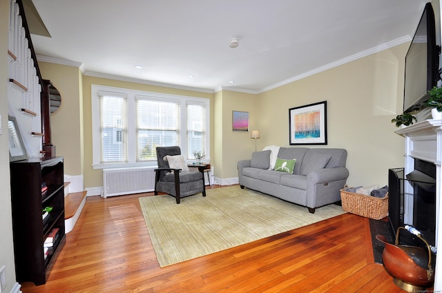 living room featuring a fireplace with raised hearth, light wood-style flooring, ornamental molding, stairway, and radiator