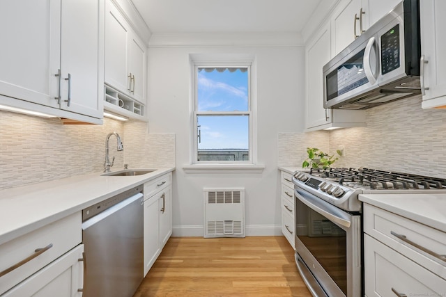 kitchen with light countertops, appliances with stainless steel finishes, white cabinets, a sink, and light wood-type flooring