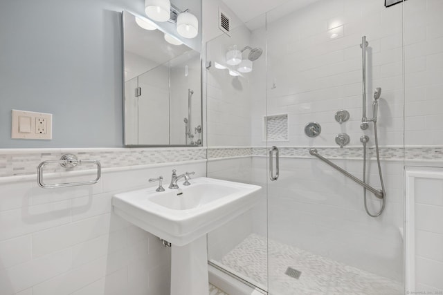 bathroom with a stall shower, a wainscoted wall, visible vents, and tile walls