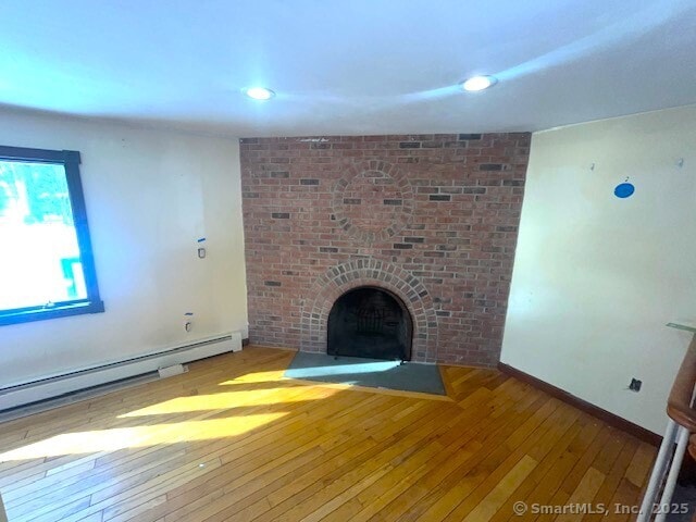 unfurnished living room featuring baseboards, wood-type flooring, baseboard heating, a brick fireplace, and recessed lighting