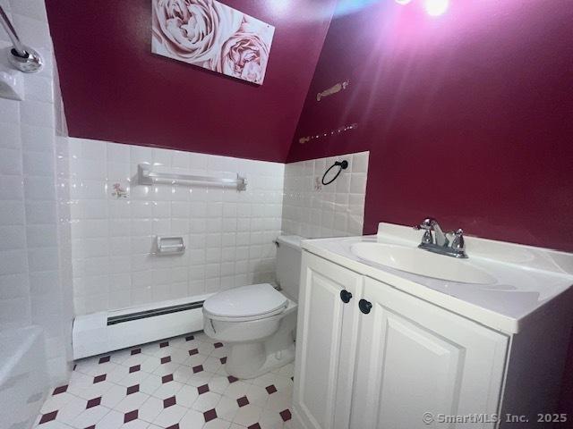 bathroom featuring toilet, a baseboard heating unit, vanity, vaulted ceiling, and walk in shower