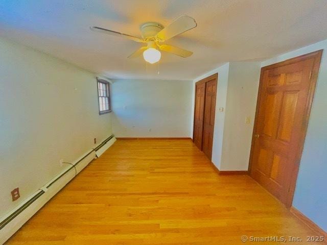 spare room featuring a baseboard radiator, baseboards, ceiling fan, and light wood finished floors