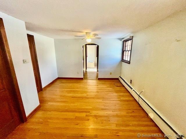 spare room featuring a ceiling fan, light wood-type flooring, baseboards, and baseboard heating