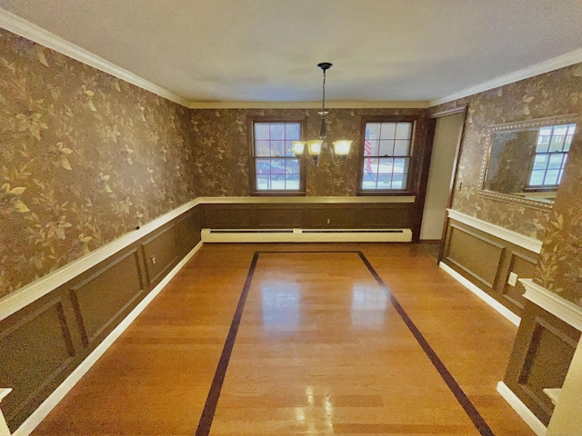 unfurnished dining area featuring an inviting chandelier, a baseboard heating unit, a healthy amount of sunlight, wainscoting, and wallpapered walls