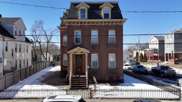 second empire-style home featuring a fenced front yard, a residential view, brick siding, and mansard roof