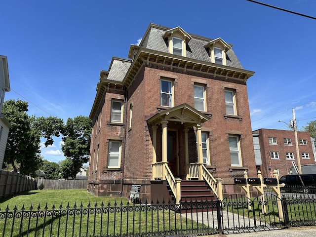 victorian home with brick siding, a front yard, mansard roof, and a fenced front yard