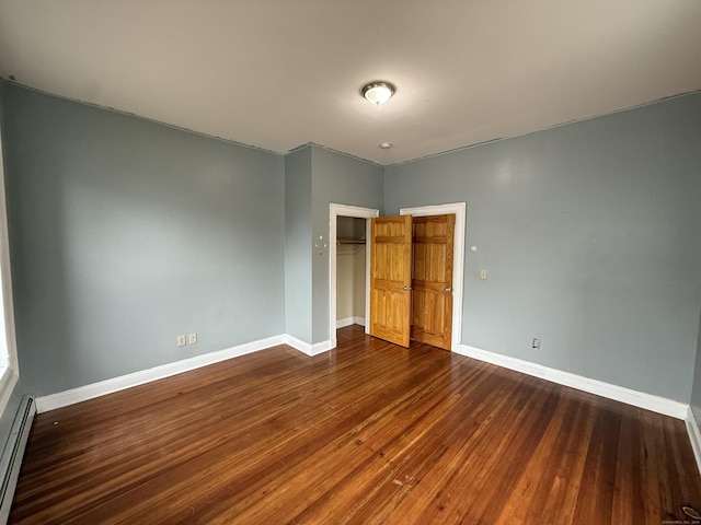 unfurnished bedroom featuring dark wood-style flooring, a closet, baseboards, and baseboard heating