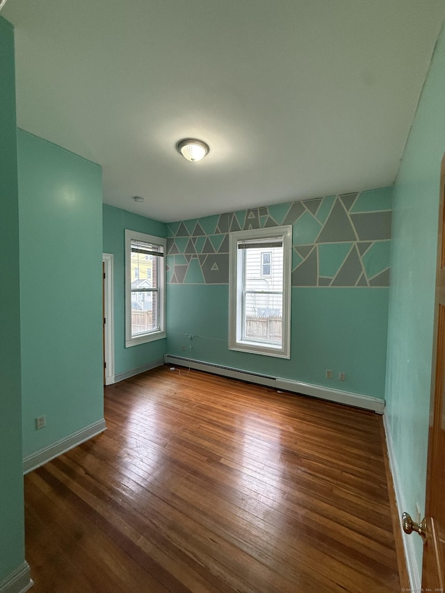 spare room with a baseboard heating unit, baseboards, and hardwood / wood-style floors