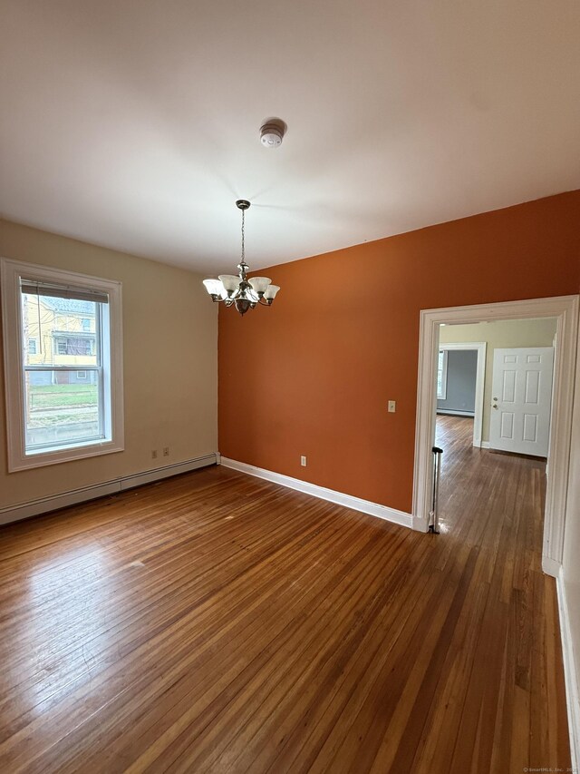 empty room with baseboard heating, a notable chandelier, dark wood-style floors, and baseboards