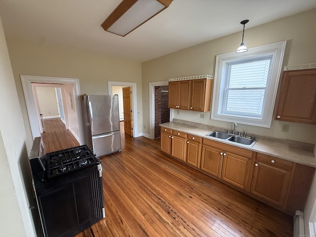 kitchen featuring a sink, light countertops, freestanding refrigerator, brown cabinetry, and wood finished floors