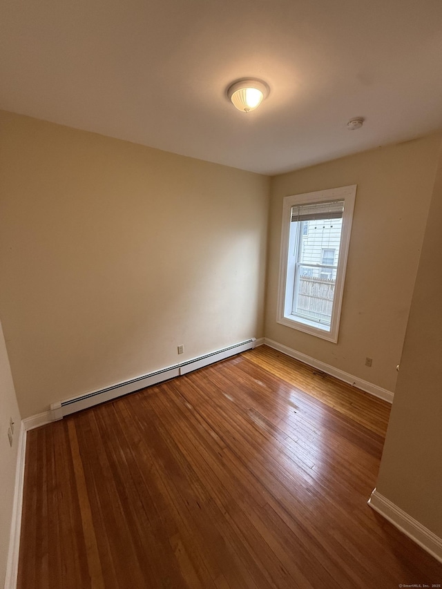 empty room with a baseboard radiator, hardwood / wood-style floors, and baseboards