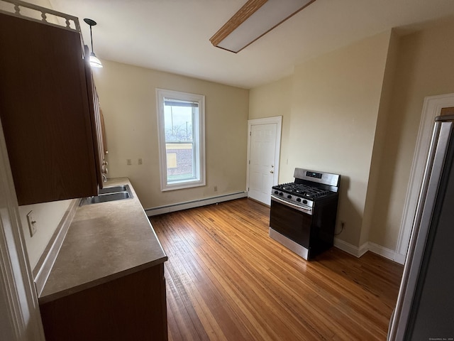 kitchen featuring appliances with stainless steel finishes, a sink, a baseboard radiator, baseboards, and hardwood / wood-style flooring