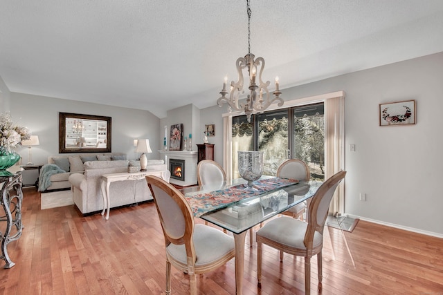 dining space featuring a notable chandelier, light wood-style flooring, a textured ceiling, a warm lit fireplace, and baseboards