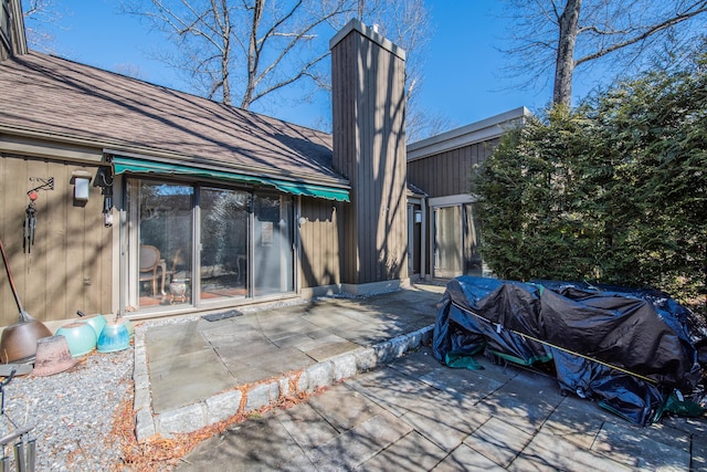 back of property with a chimney, roof with shingles, and a patio area