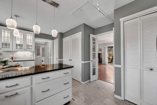 kitchen featuring dark stone counters, white cabinets, decorative backsplash, glass insert cabinets, and pendant lighting