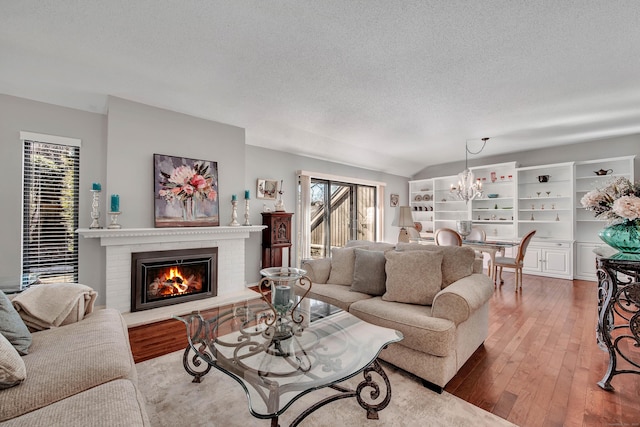 living area featuring a textured ceiling, hardwood / wood-style floors, a brick fireplace, and an inviting chandelier