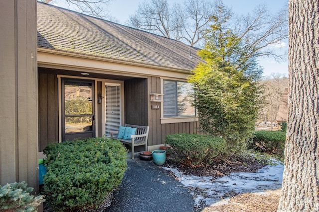 view of exterior entry with covered porch, a shingled roof, and board and batten siding