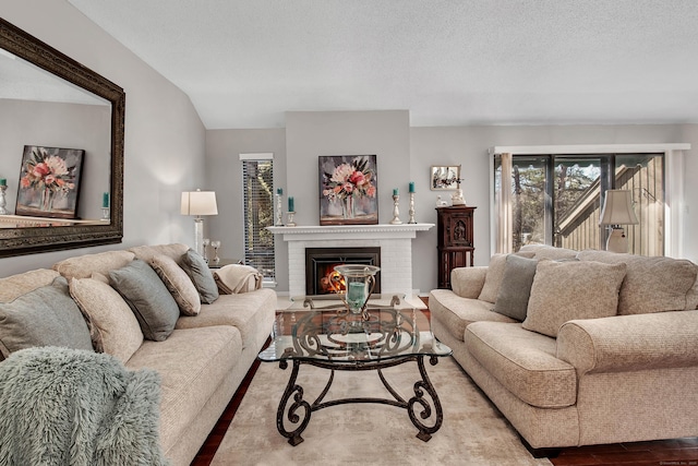 living room with a brick fireplace, a textured ceiling, vaulted ceiling, and wood finished floors