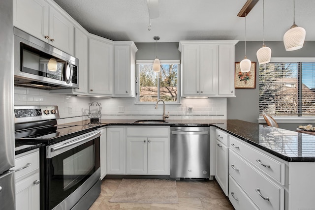 kitchen featuring stainless steel appliances, backsplash, white cabinetry, a sink, and a peninsula