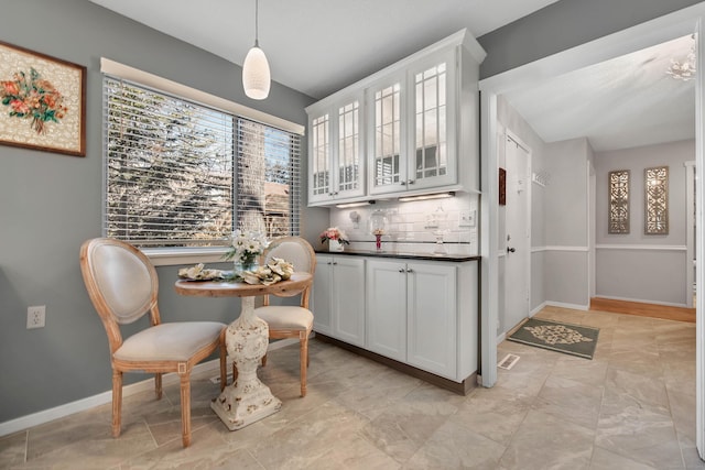 kitchen with baseboards, white cabinets, backsplash, dark countertops, and glass insert cabinets