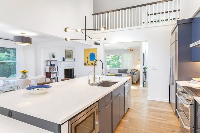 kitchen featuring a fireplace, a sink, light wood-style floors, open floor plan, and appliances with stainless steel finishes