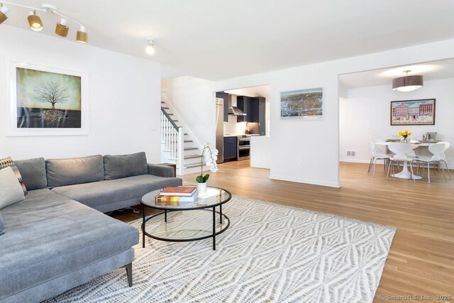 living area with visible vents, light wood-style flooring, baseboards, and stairs