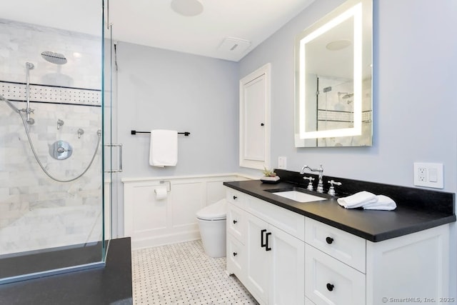 bathroom featuring toilet, a decorative wall, vanity, wainscoting, and a stall shower