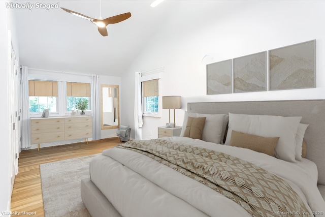 bedroom featuring light wood-style floors, lofted ceiling, multiple windows, and a ceiling fan