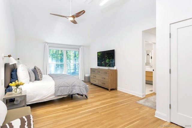 bedroom featuring connected bathroom, a ceiling fan, baseboards, a towering ceiling, and light wood-style floors