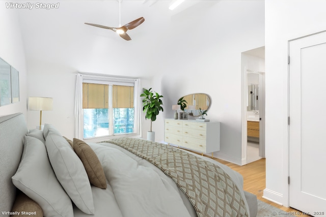 bedroom featuring a towering ceiling, light wood finished floors, ensuite bath, and baseboards