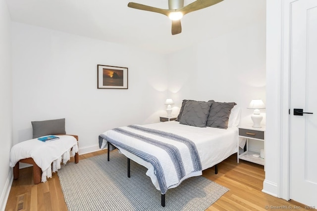 bedroom featuring a ceiling fan, visible vents, baseboards, and wood finished floors