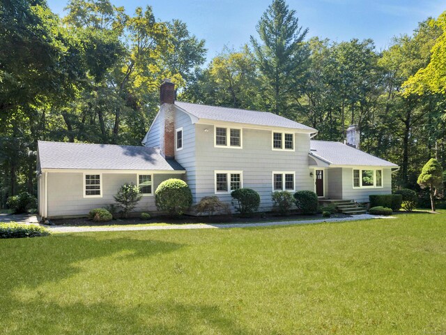 view of front of house with a chimney, a front lawn, and roof with shingles