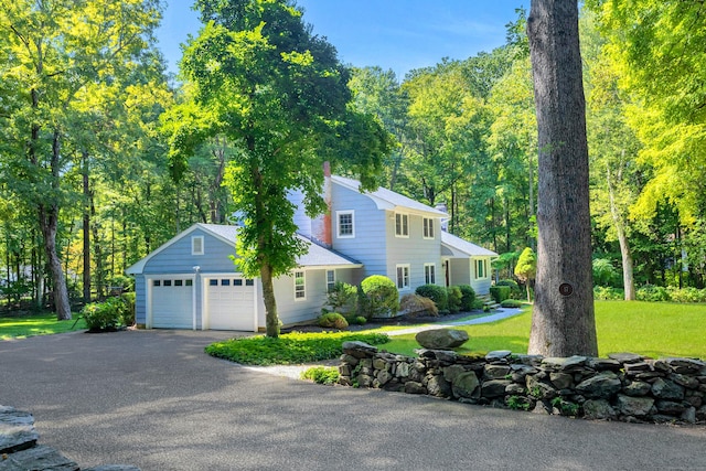 view of front facade featuring aphalt driveway, a chimney, a front yard, a garage, and a forest view