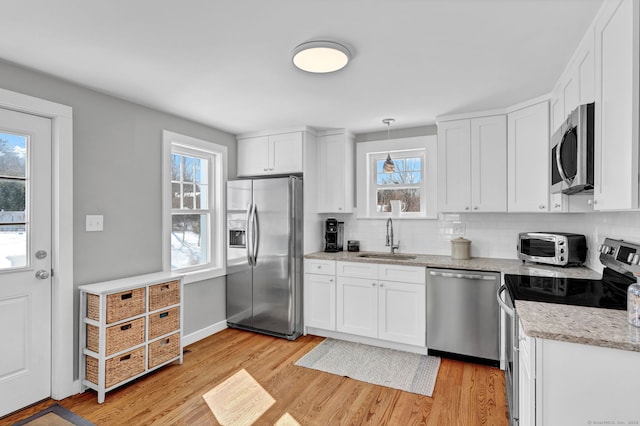 kitchen featuring decorative backsplash, light wood-style flooring, appliances with stainless steel finishes, white cabinetry, and a sink