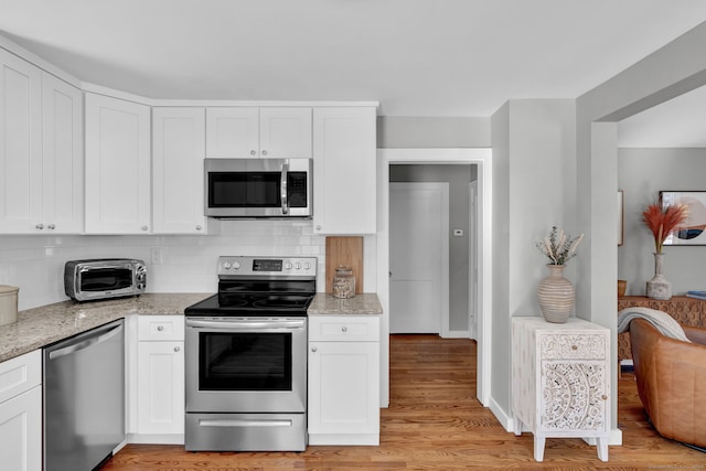 kitchen with appliances with stainless steel finishes, a toaster, white cabinetry, and backsplash