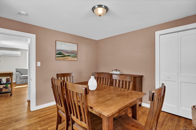 dining area featuring an AC wall unit, light wood-style flooring, and baseboards