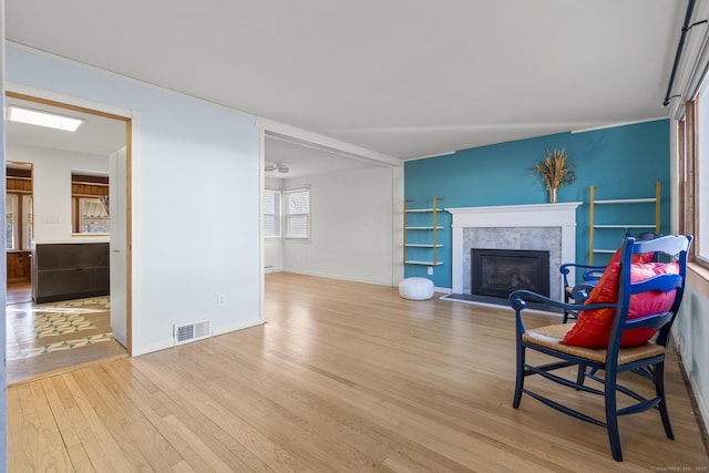 living area with a tile fireplace, visible vents, baseboards, and wood finished floors