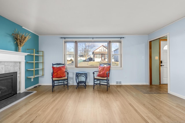 living area with a tile fireplace, visible vents, baseboards, and wood finished floors