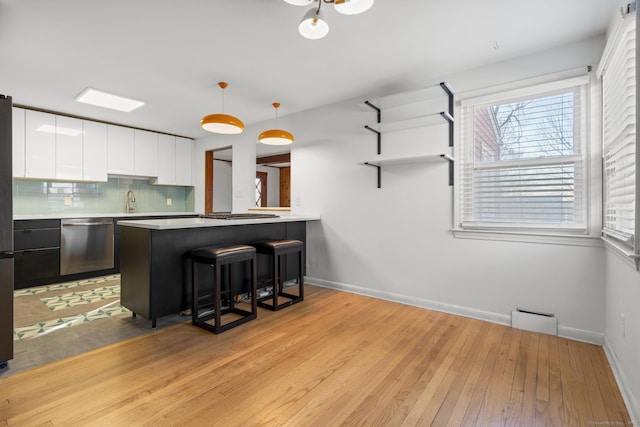 kitchen with a breakfast bar, white cabinets, light wood finished floors, stainless steel dishwasher, and tasteful backsplash