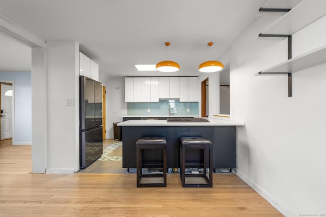 kitchen featuring light wood finished floors, tasteful backsplash, freestanding refrigerator, white cabinetry, and a peninsula