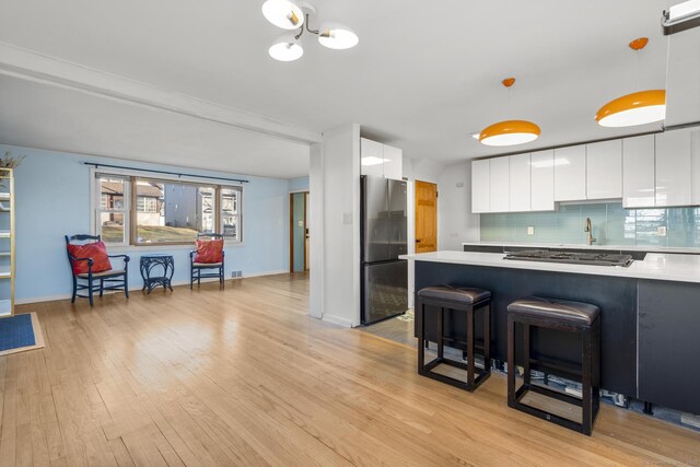 kitchen with tasteful backsplash, white cabinets, light wood-style flooring, appliances with stainless steel finishes, and light countertops