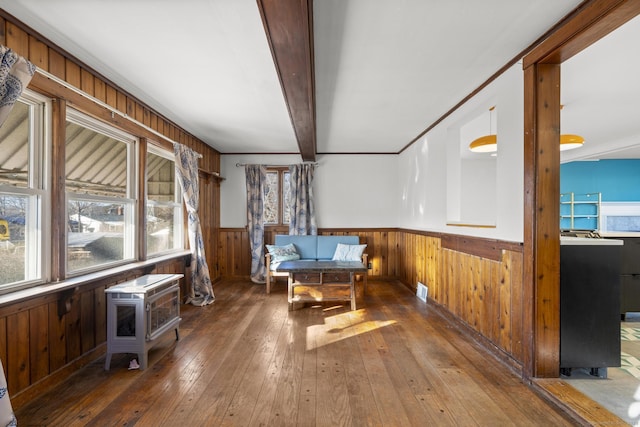 living area featuring a wainscoted wall, wood-type flooring, a wood stove, wood walls, and beam ceiling