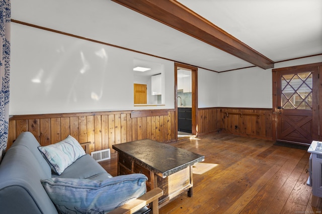 living area with a wainscoted wall, visible vents, beam ceiling, and hardwood / wood-style floors