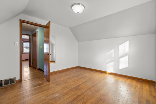 additional living space with vaulted ceiling, wood-type flooring, visible vents, and baseboards