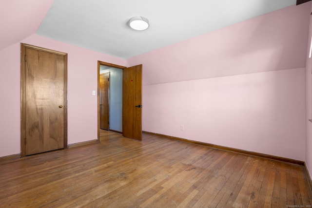 unfurnished bedroom with lofted ceiling, wood-type flooring, and baseboards