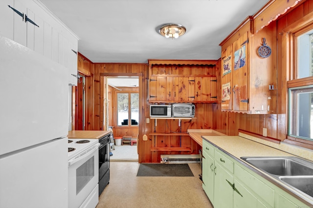 kitchen with light countertops, green cabinets, a sink, wooden walls, and white appliances